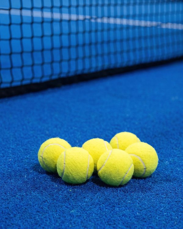 Varias pelotas de pádel sobre el césped azul junto a la red