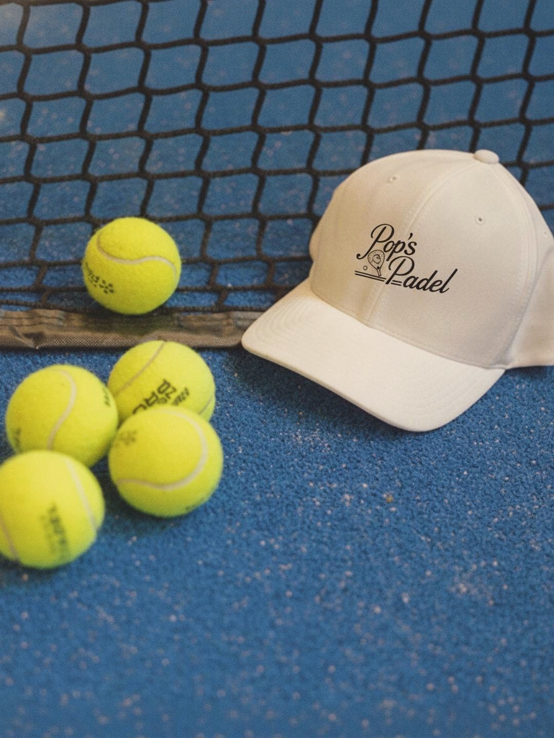 Pop's Padel cap and four padel balls on the turf