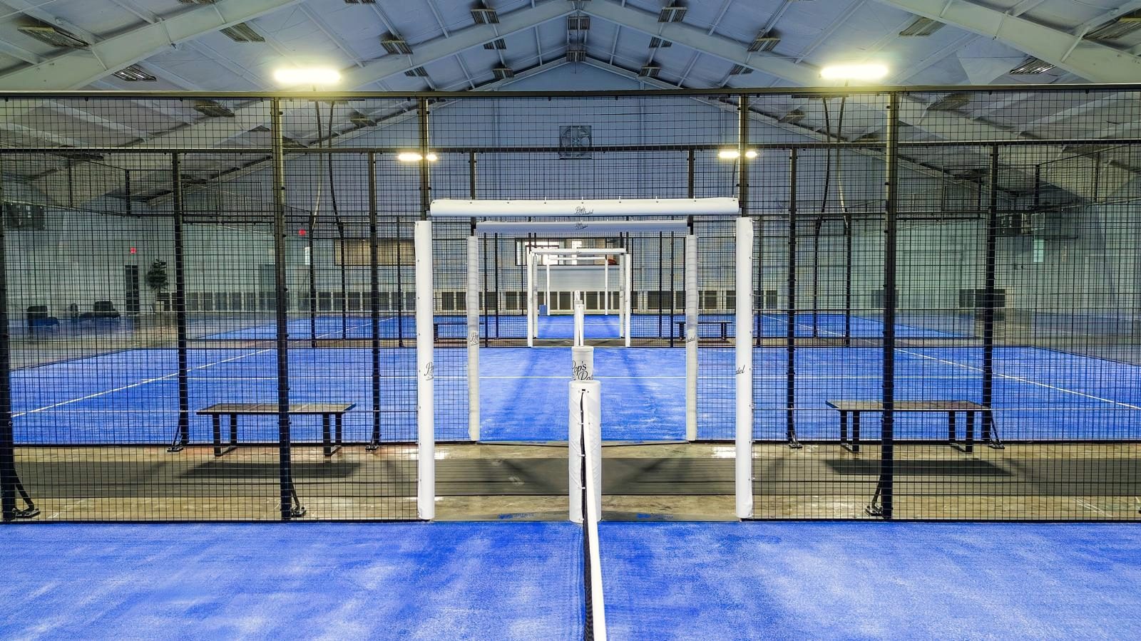 Las pistas panorámicas de Pop's Padel en fila, vistas a través de los postes de la red