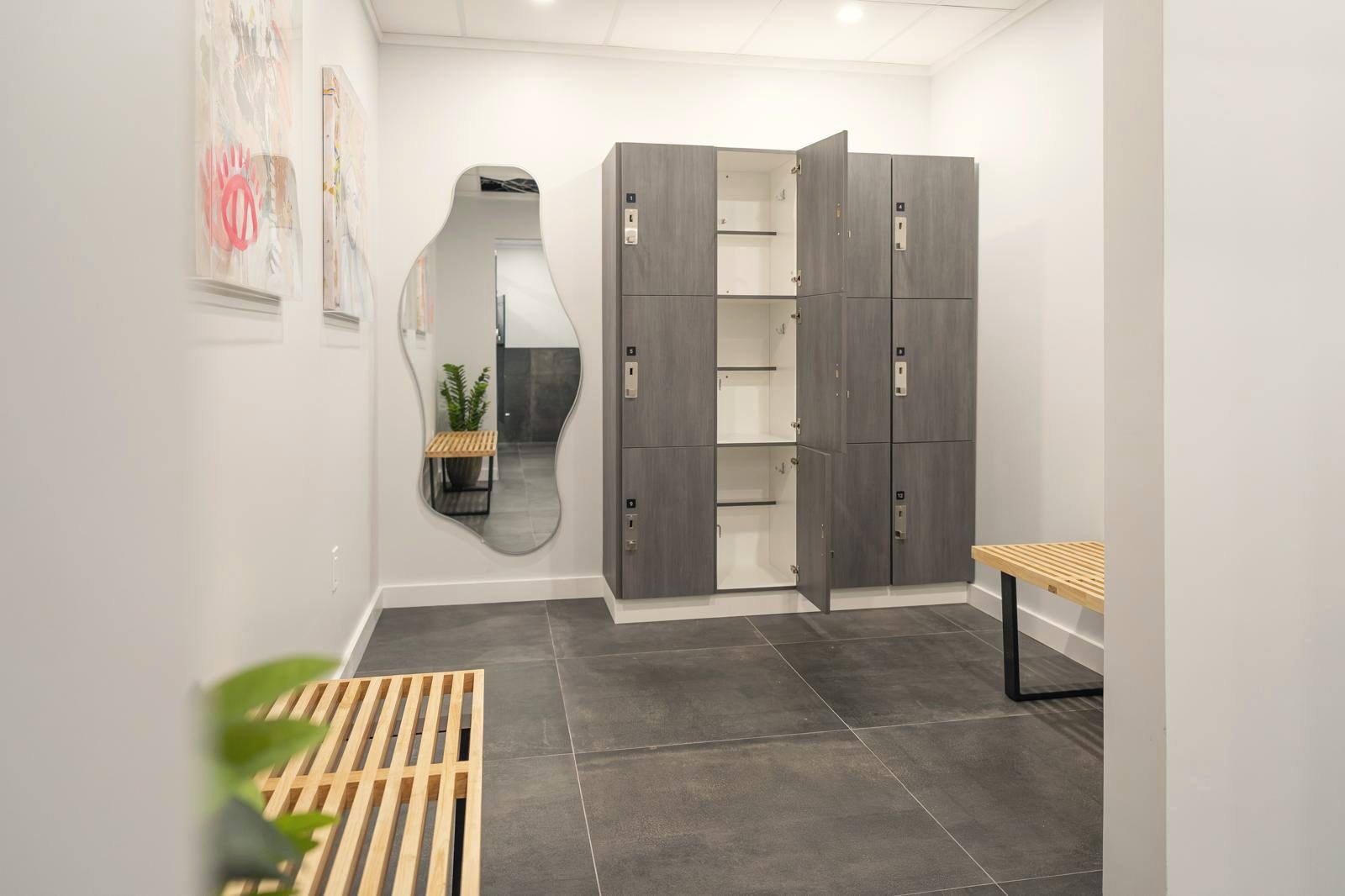Vestuario con bancos de madera, taquillas y un espejo de formas orgánicas