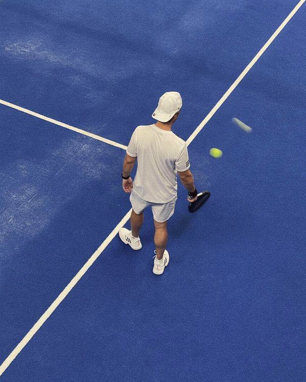 Un jugador vestido de blanco rematando sobre el césped azul, visto desde arriba
