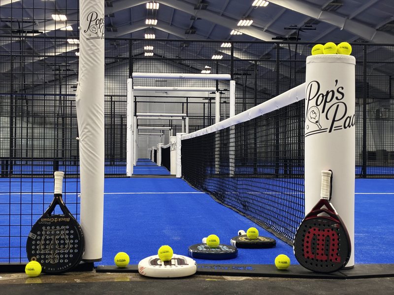 Palas y pelotas alineadas junto a un poste de red con el logo de Pop's Padel