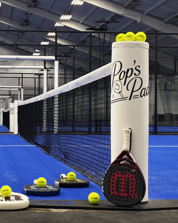Palas y pelotas alineadas junto al poste de la red, listas para jugar